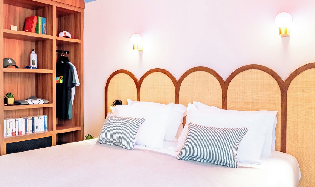 Una cama bien hecha con ropa de cama blanca y almohadas a rayas, una estantería de madera con diversos objetos y un cabecero de diseño único.