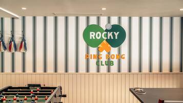 A foosball table and a ping pong table in a room with striped walls and a logo for Rocky Ping Pong Club.