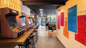 A retro arcade with wooden cabinets and neon signs, a bar area with stools, and posters on the wall. - RockyPop Marseille hôtel (Marseille)