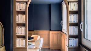 A cozy reading nook with a wooden bench and bookshelves filled with books, a window for natural light, and a dark blue accent wall. - RockyPop Marseille hôtel (Marseille)