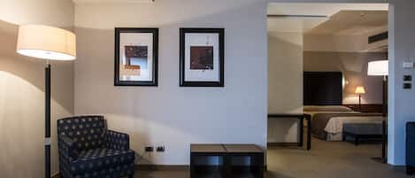 Habitación de hotel con una silla, una mesita, dos cuadros en la pared, una cama y una lámpara.