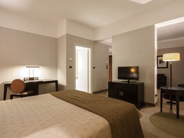 Una camera d'albergo con un letto, una scrivania con una lampada, una televisione e una sedia.