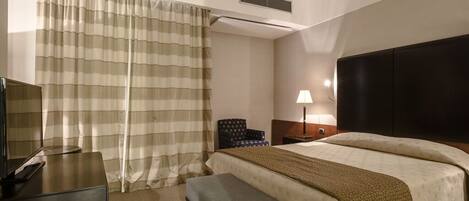 Una habitación de hotel con una cama, un escritorio, una silla, una lámpara y un televisor.