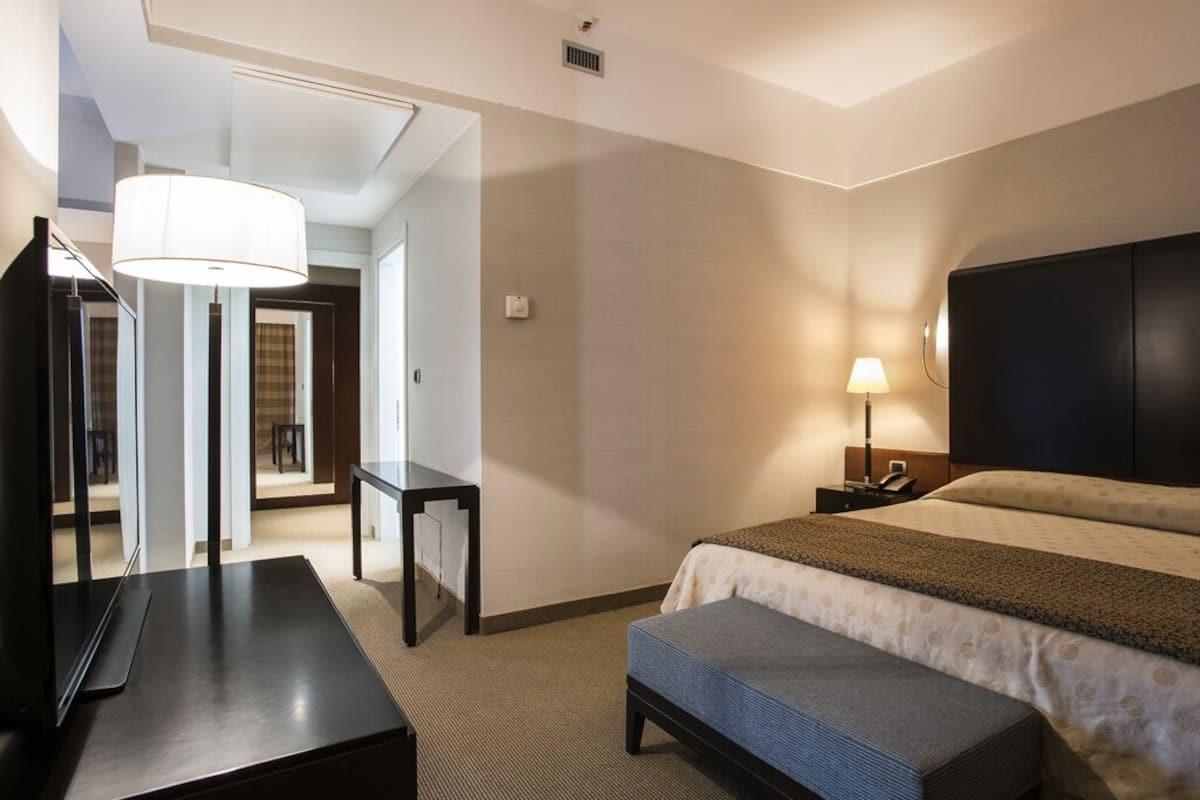 A hotel room with a bed, bedside table, lamp, and a large mirror.