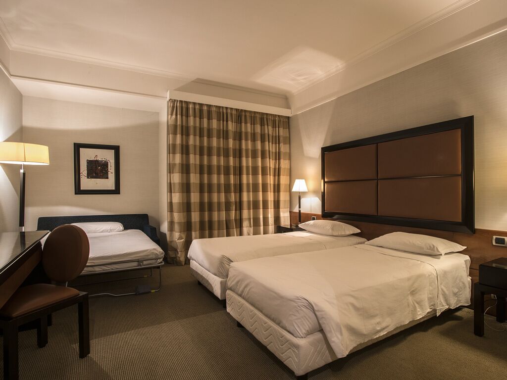 A hotel room with two beds, a desk, a chair, a lamp, and a picture on the wall.