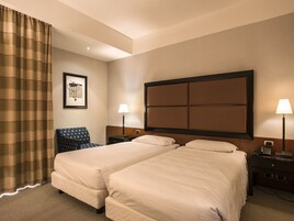 Een hotelkamer met twee bedden, een stoel, een nachtkastje met lamp en een lijst aan de muur.