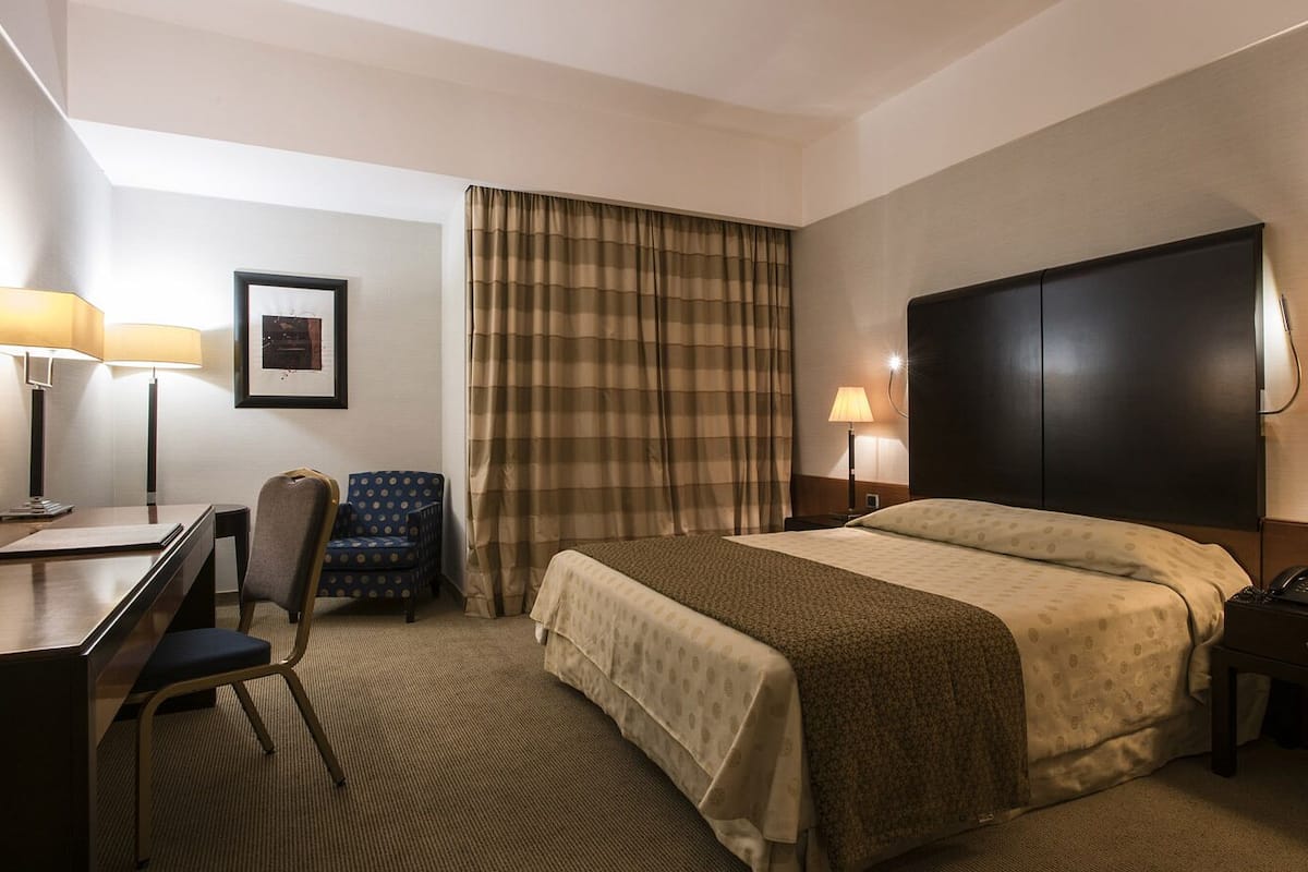 A hotel room with a bed, desk, chair, and two bedside lamps.