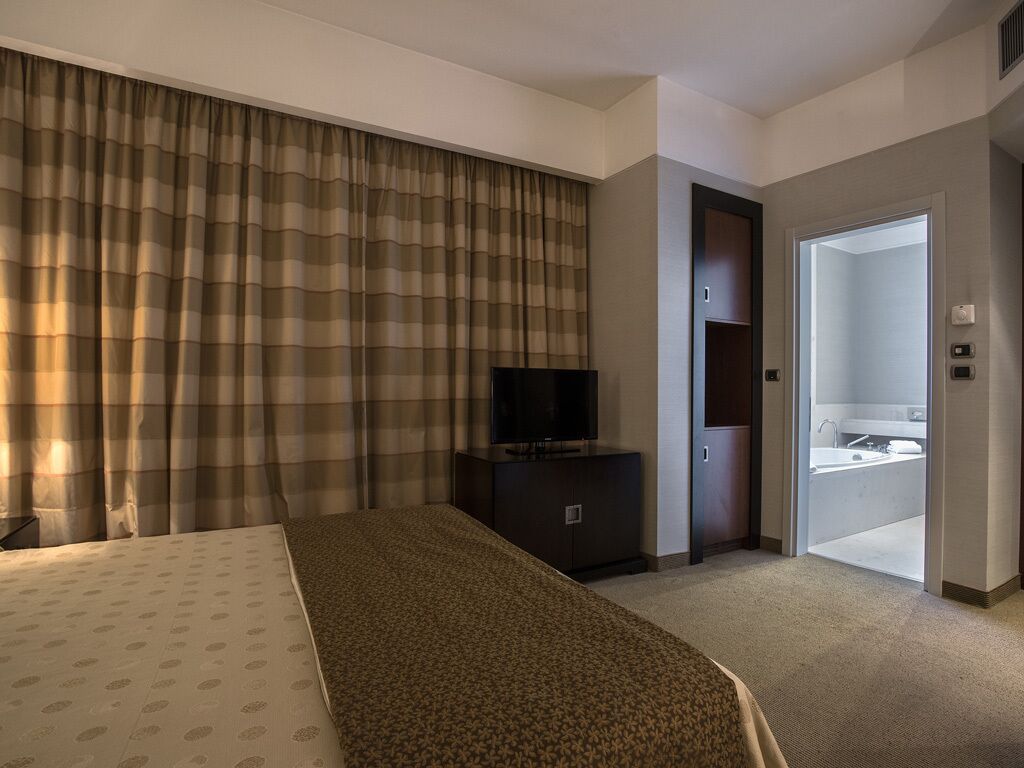 A hotel room with a bed, a television on a dresser, and a bathroom visible through an open door.