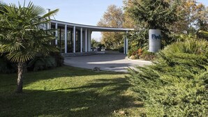 Un edificio moderno con fachada de vidrio, rodeado de vegetación cuidada y un cielo despejado.