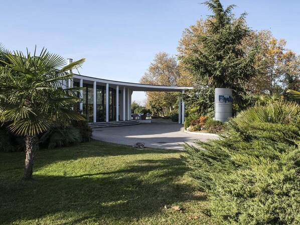 A modern building with a glass facade, surrounded by well-maintained greenery and a clear sky. - Fly On Hotel (Bologna)