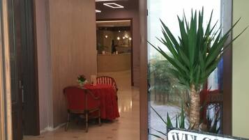 Un'area della reception di un hotel con un cartello che dice 'WELCOME', una scrivania della reception, una sala da pranzo con un tavolo e sedie rossi e una pianta in vaso.