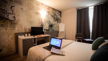 A hotel room with a bed, a desk with a laptop, a television, and a chair.