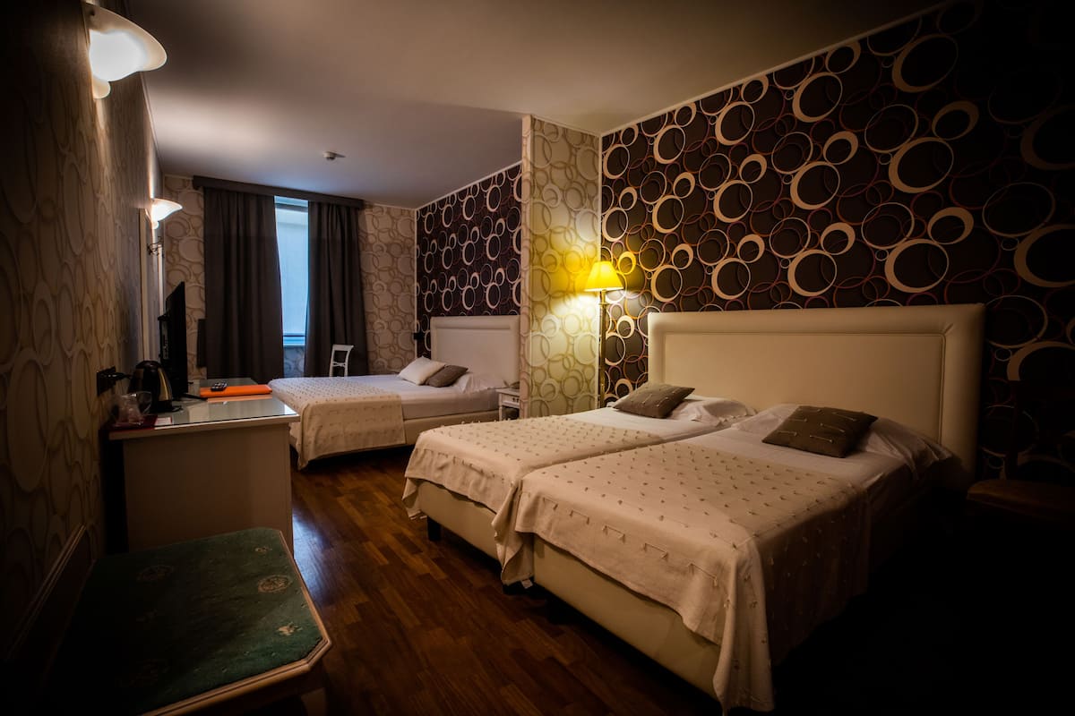 A hotel room with two beds, a desk, a chair, and a lamp.