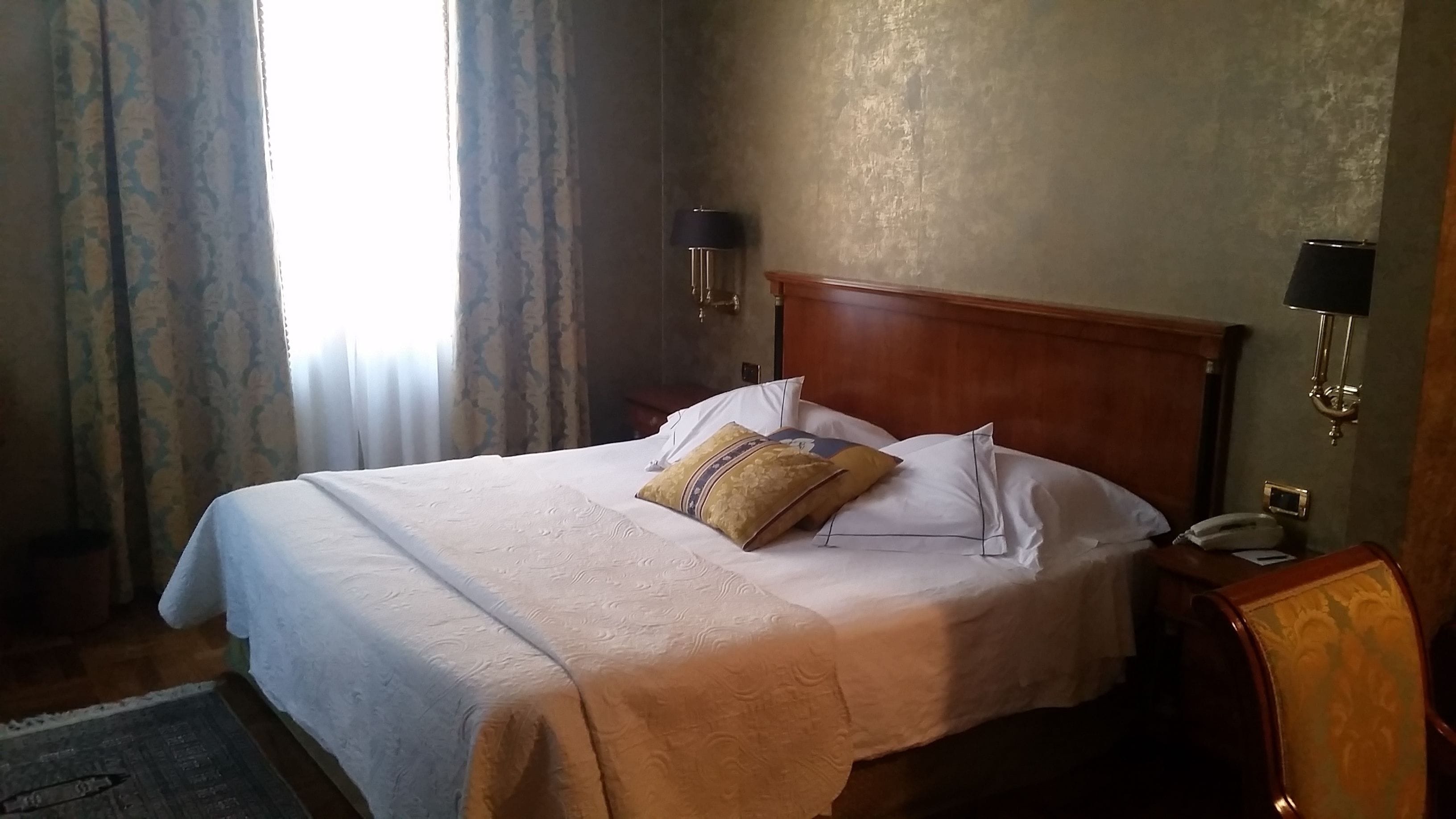 Ein Hotelzimmer mit einem großen Bett, zwei Nachttischlampen, einem Holz-Kopfschild und einem Nachttisch mit Telefon.