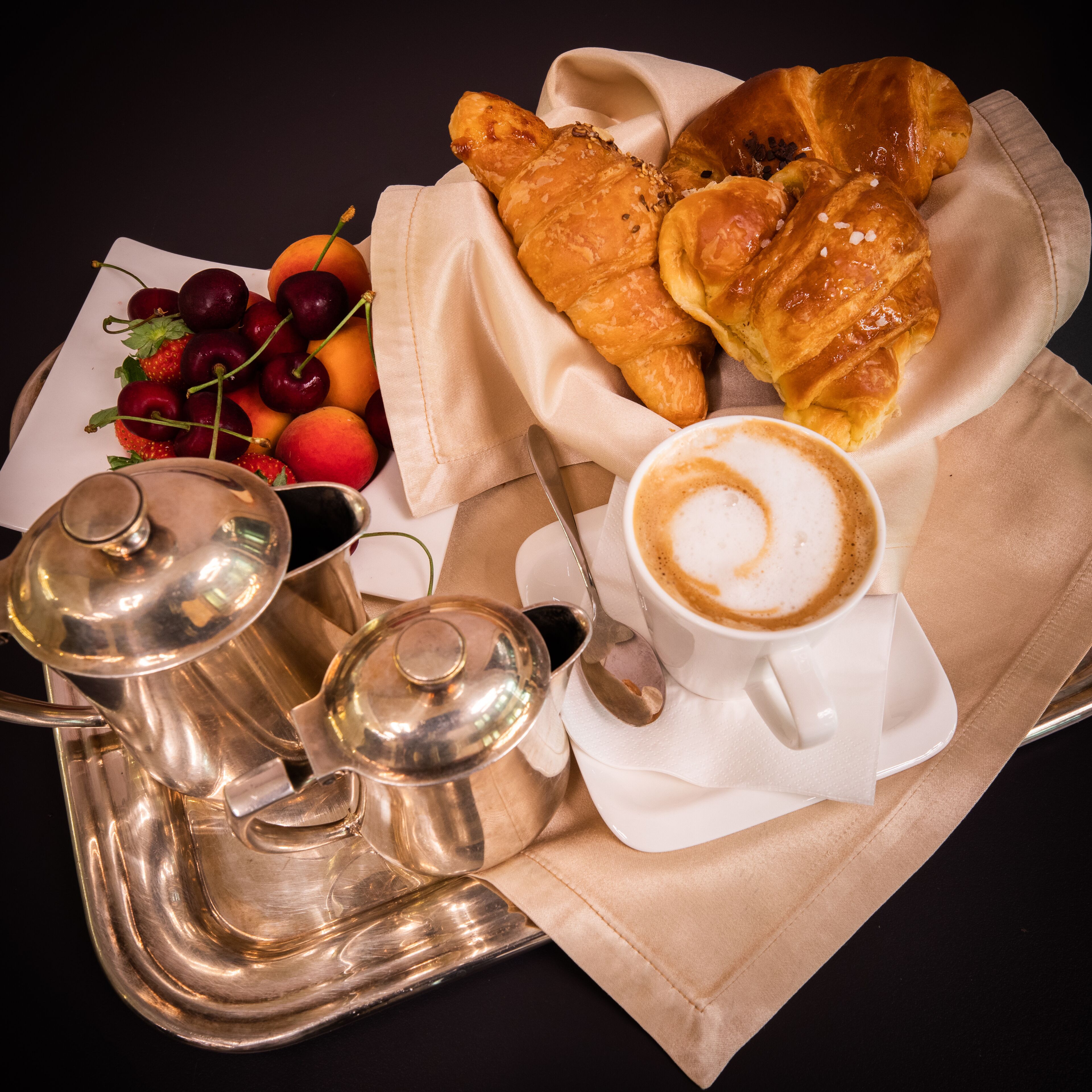 Un plateau avec des croissants, des cerises et une tasse de café.