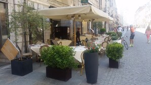 An outdoor cafe with tables and chairs, potted plants, and a covered seating area. - Hotel Palazzo Lovera (Cuneo)