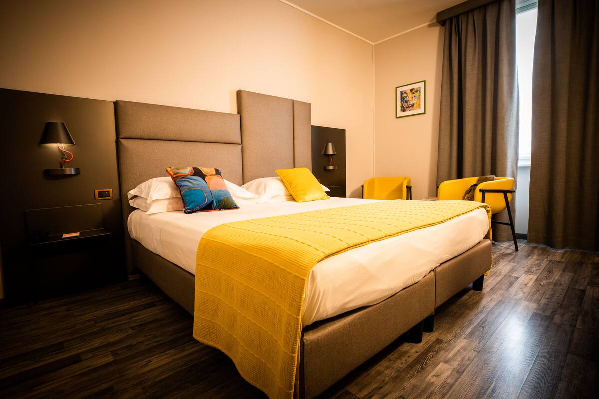 A hotel room with a large bed, a bedside table, a chair, and a window with curtains.