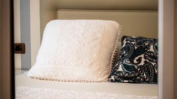 Un letto con una testiera trapuntata bianca e un cuscino decorato, su uno sfondo di parete a righe.