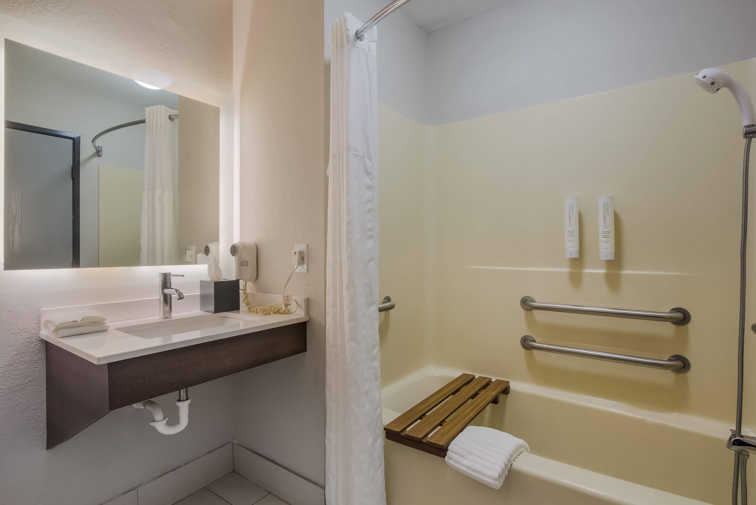 Un baño con lavamanos, espejo, ducha y toallero.