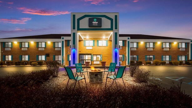 Un hôtel Clarion Pointe avec une façade en briques, une entrée centrale et un espace agrémenté d’un foyer et de chaises.