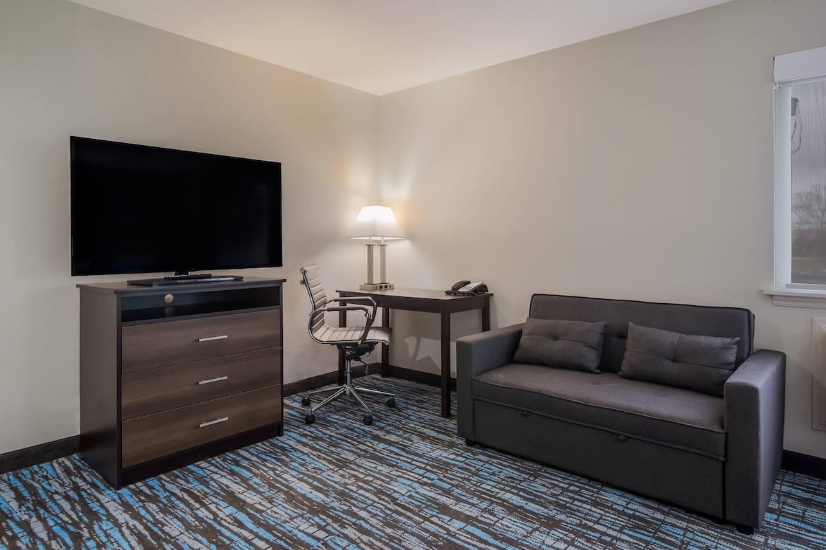 A hotel room with a flat-screen TV, a desk with a lamp, a chair, and a sofa.