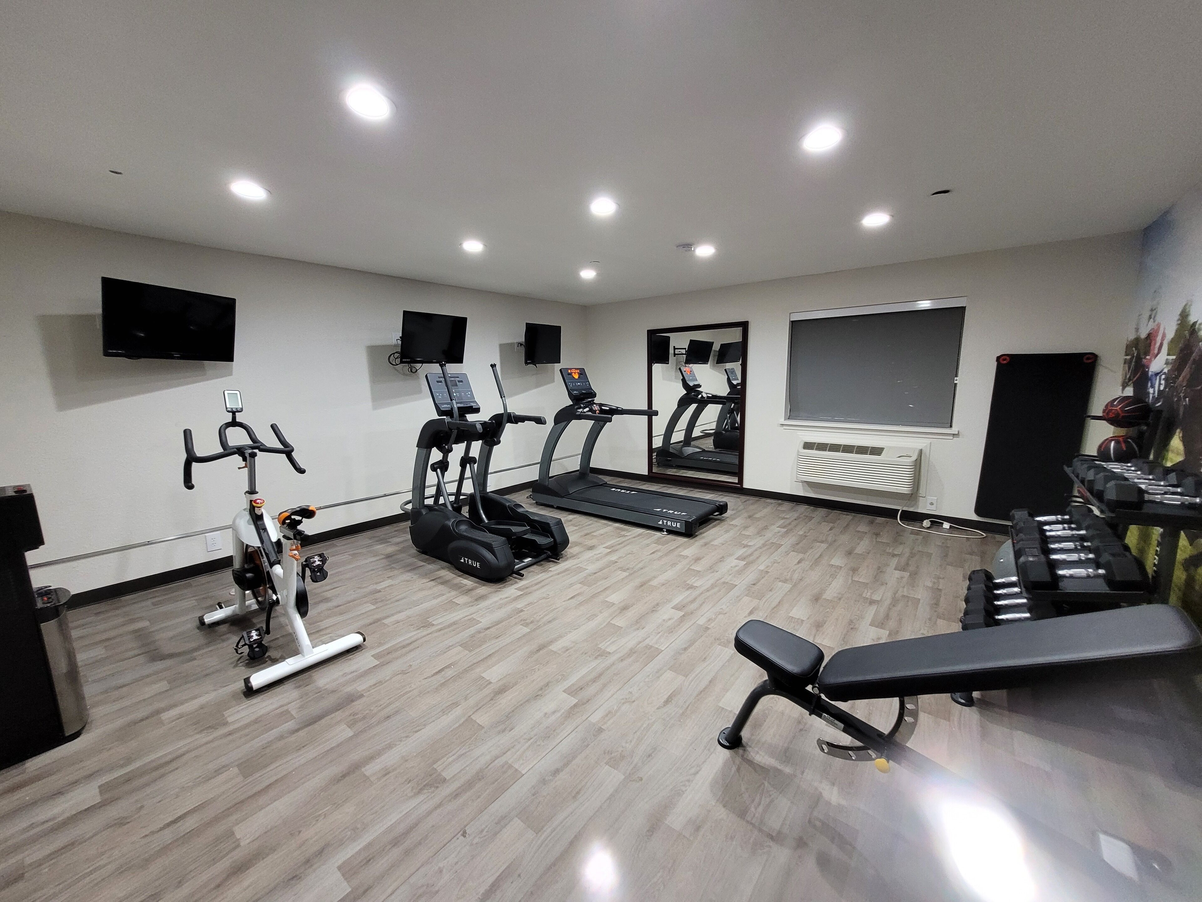 Un gimnasio con cintas de correr, elíptica, bicicleta estática y banco.