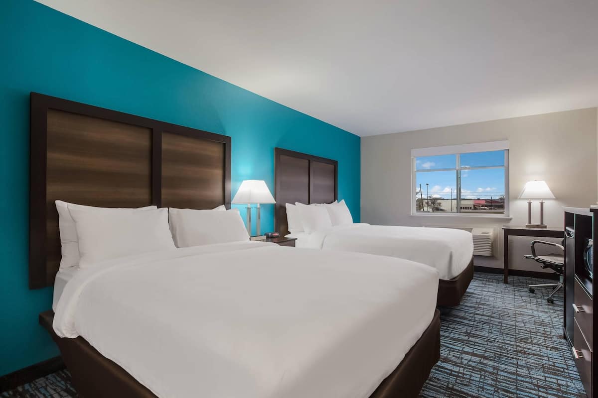 A hotel room with two beds, a desk, a chair, a window with a view, and a lamp.