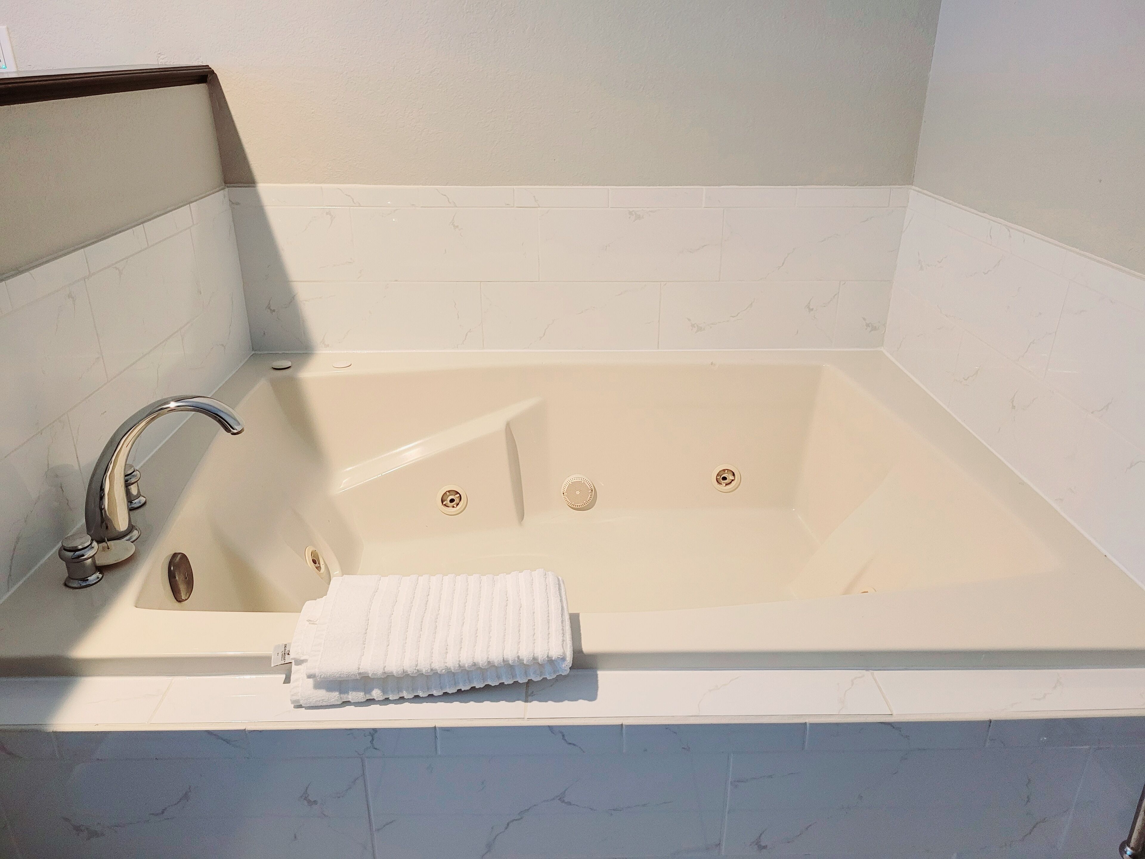 Una bañera rectangular con un solo grifo y dos desagües, una toalla blanca al lado, y un revestimiento de pared con diseño de mármol.
