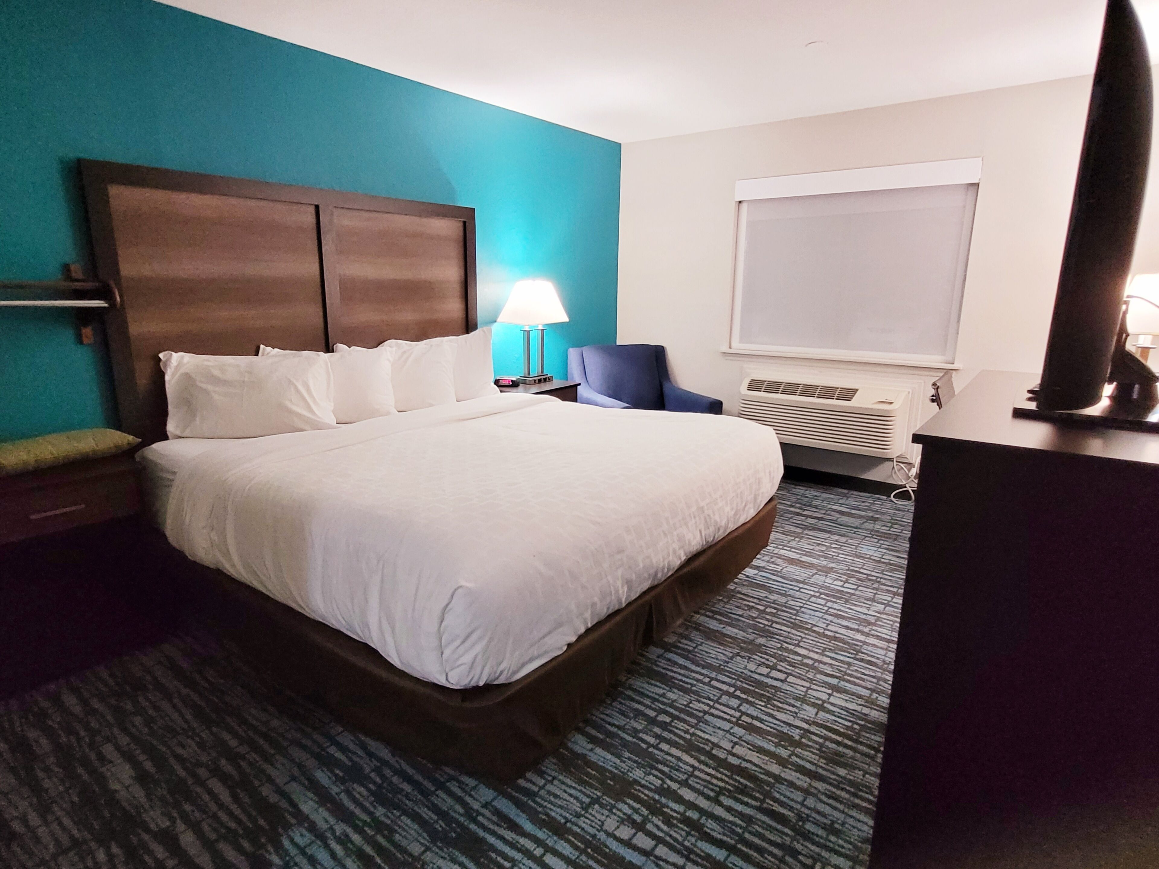 Habitación de hotel con una cama grande, un escritorio, una silla, una lámpara y un equipo de aire acondicionado.