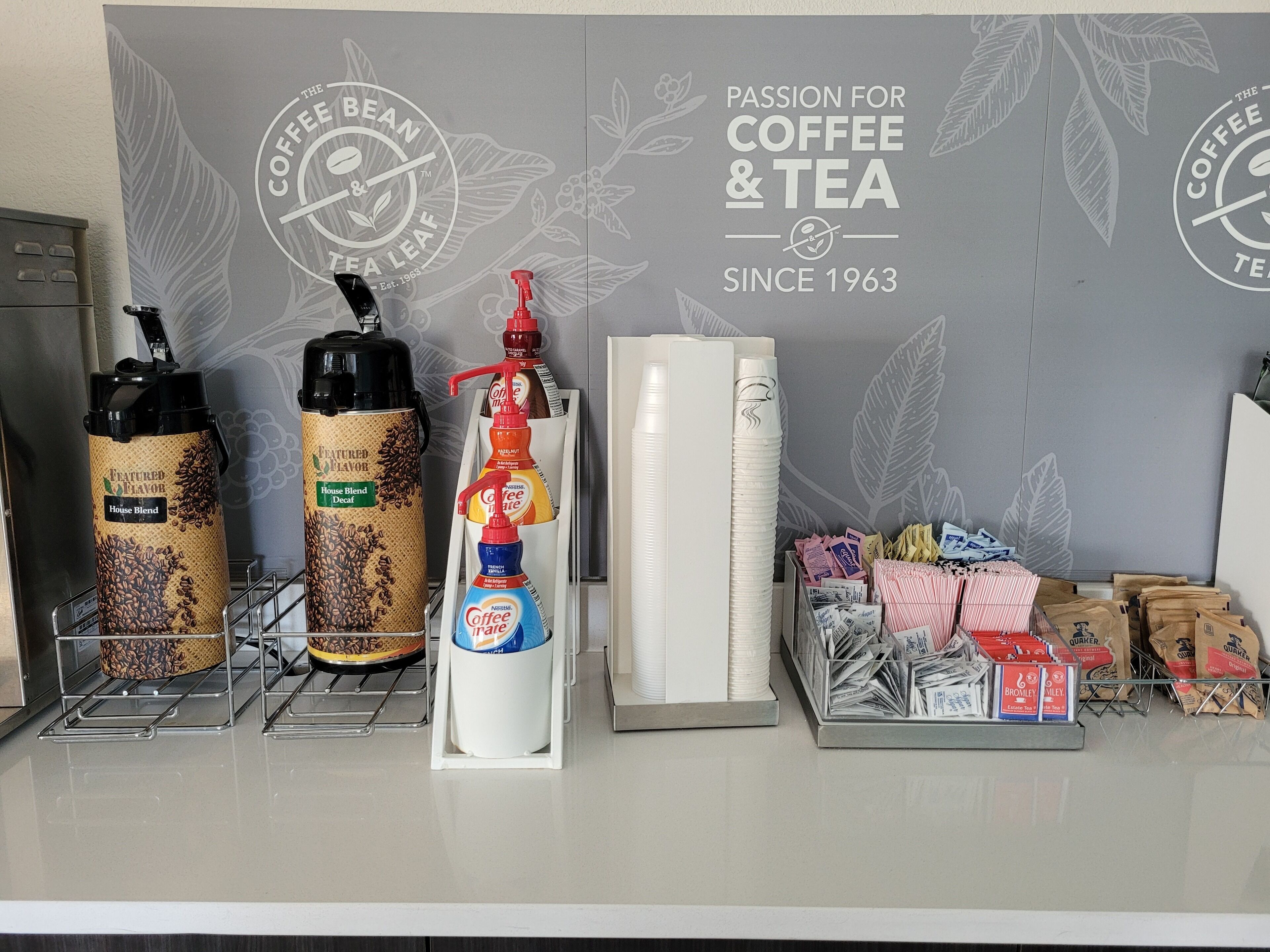 A coffee shop counter with various coffee and tea products, including branded thermos flasks, a coffee dispenser, and packaged tea bags.