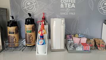 A coffee shop counter with various coffee and tea products, including branded thermos flasks, a coffee dispenser, and packaged tea bags.