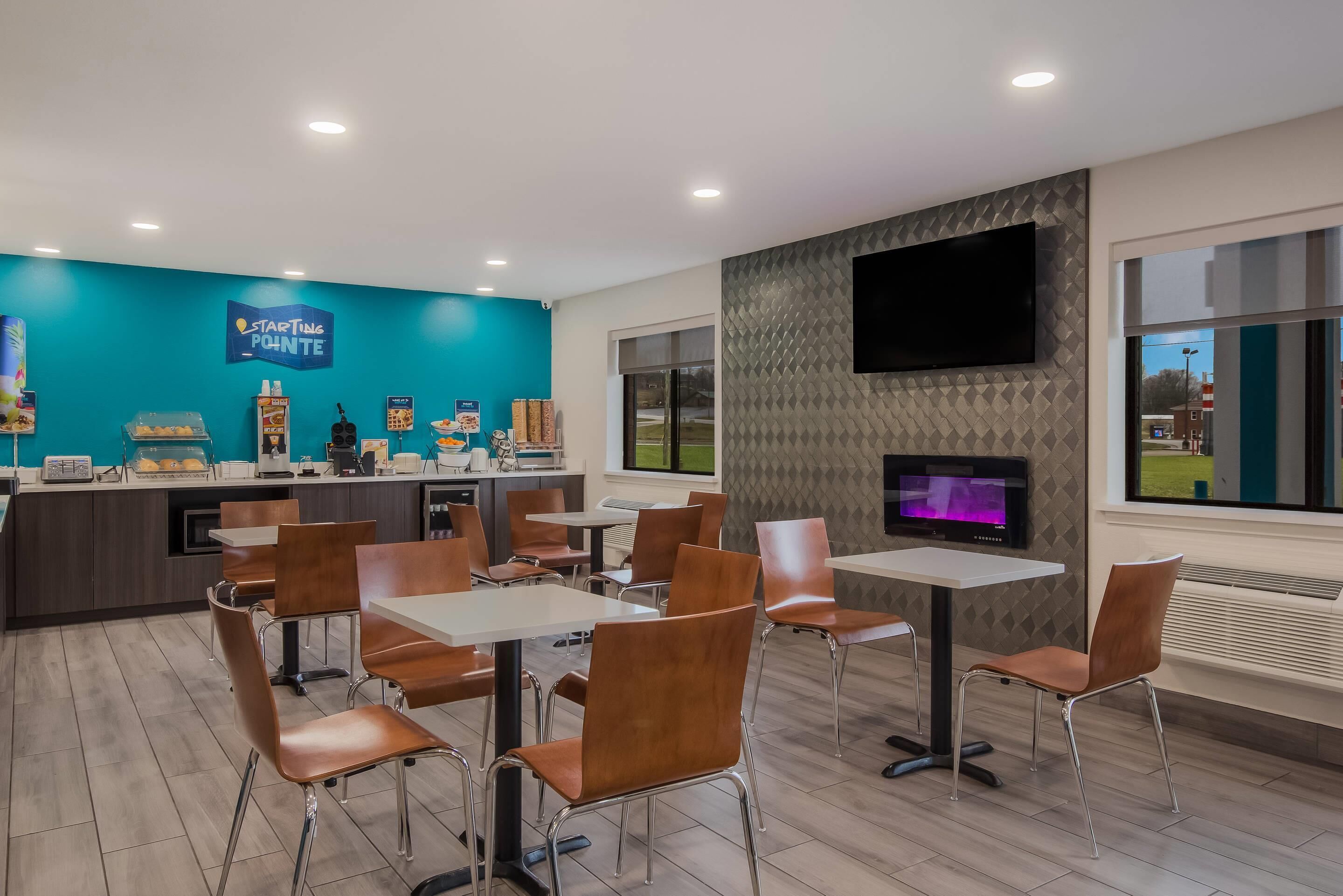 A modern dining area with tables and chairs, a counter with food items, and a TV mounted on the wall.