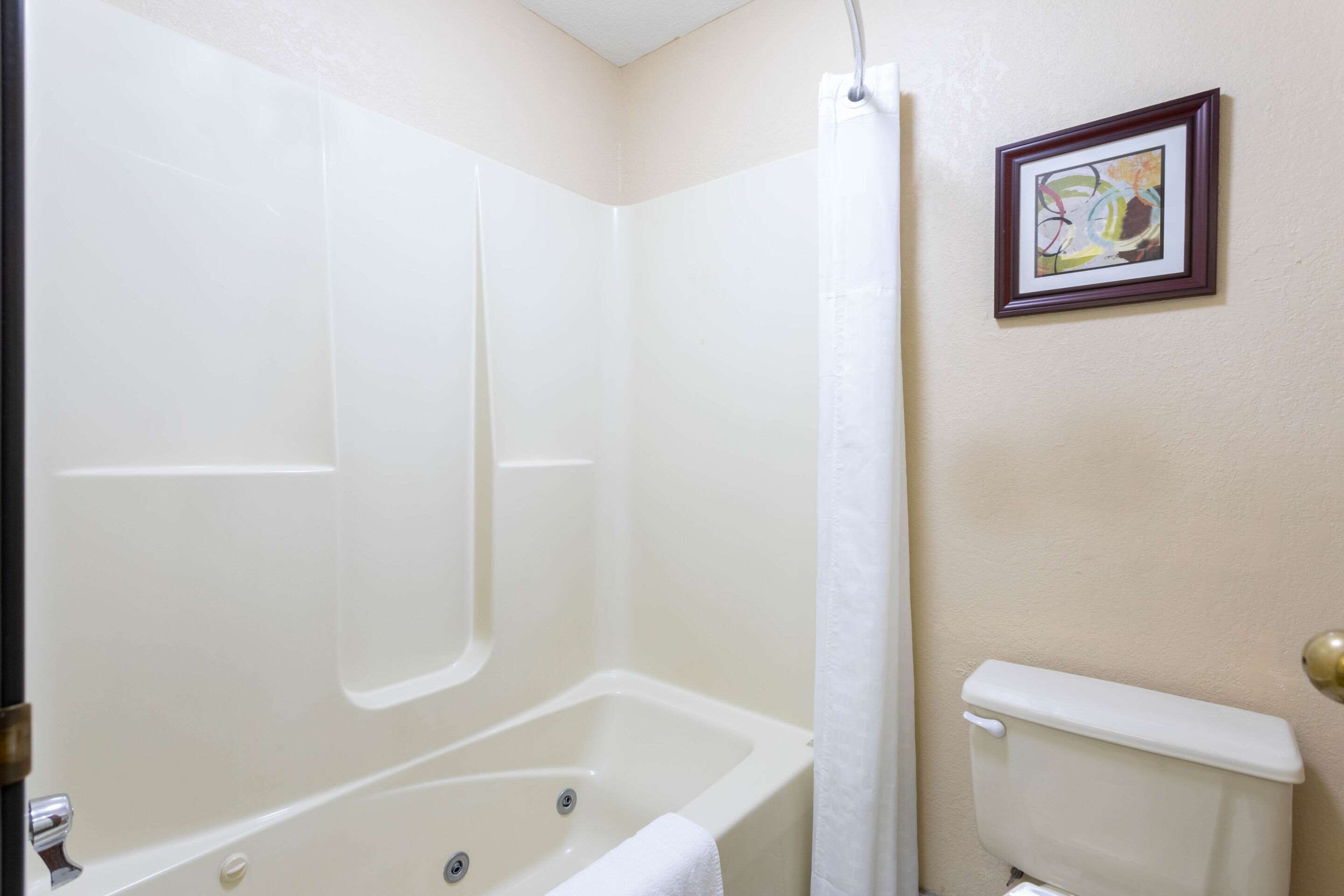 A bathroom with a bathtub, toilet, and a framed picture on the wall.