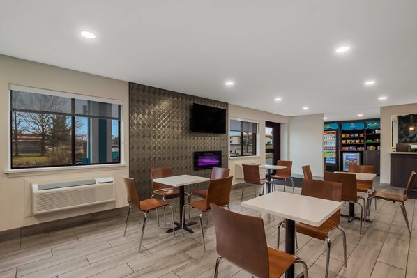 A modern restaurant with tables and chairs, a flat-screen TV mounted on the wall, and a vending machine in the background.