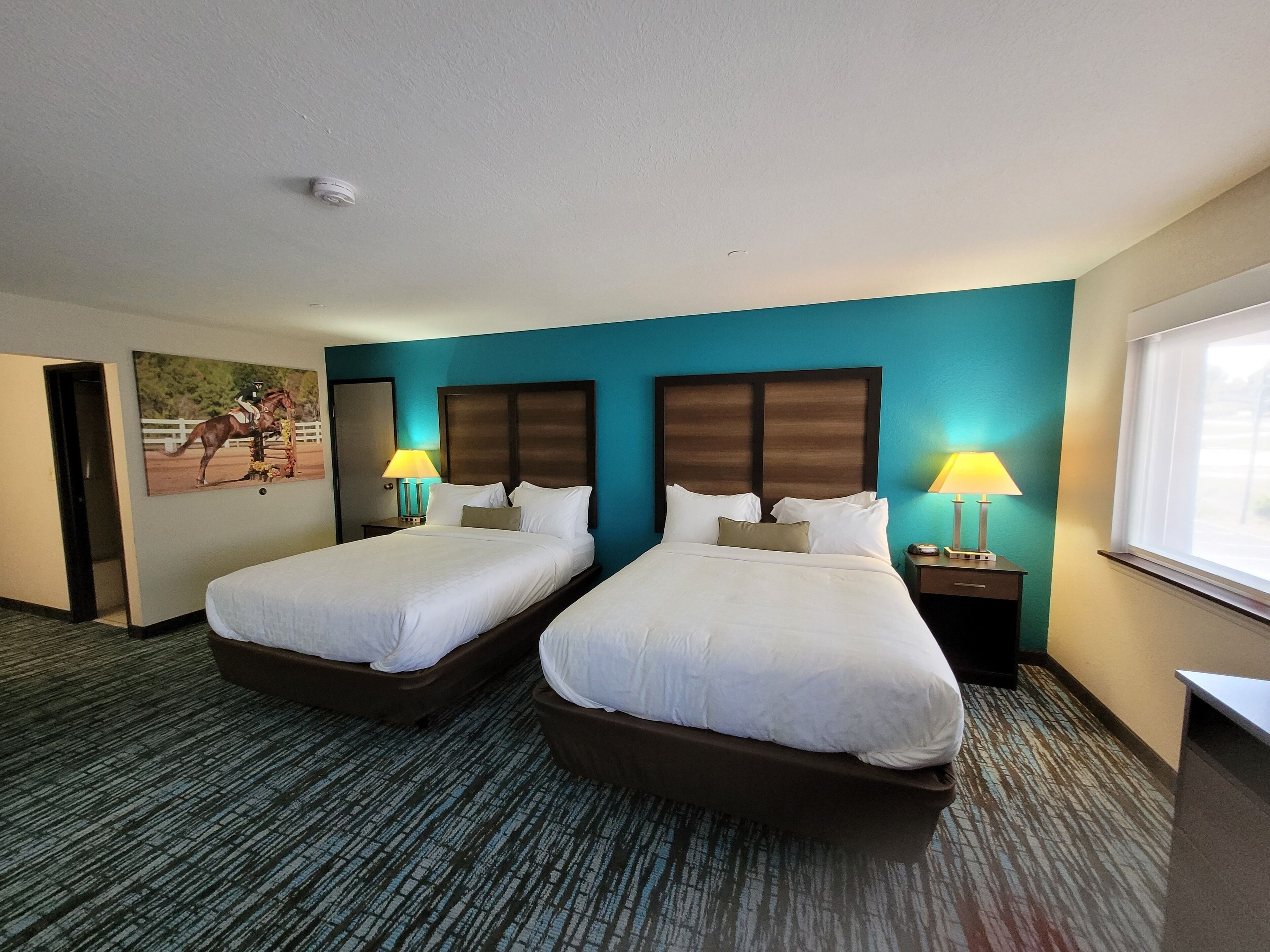 A hotel room with two beds, a painting on the wall, and a window.