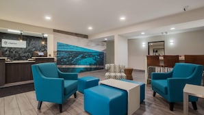 Un hall d’hôtel avec des sièges bleus, un comptoir d’accueil et une grande fresque murale.