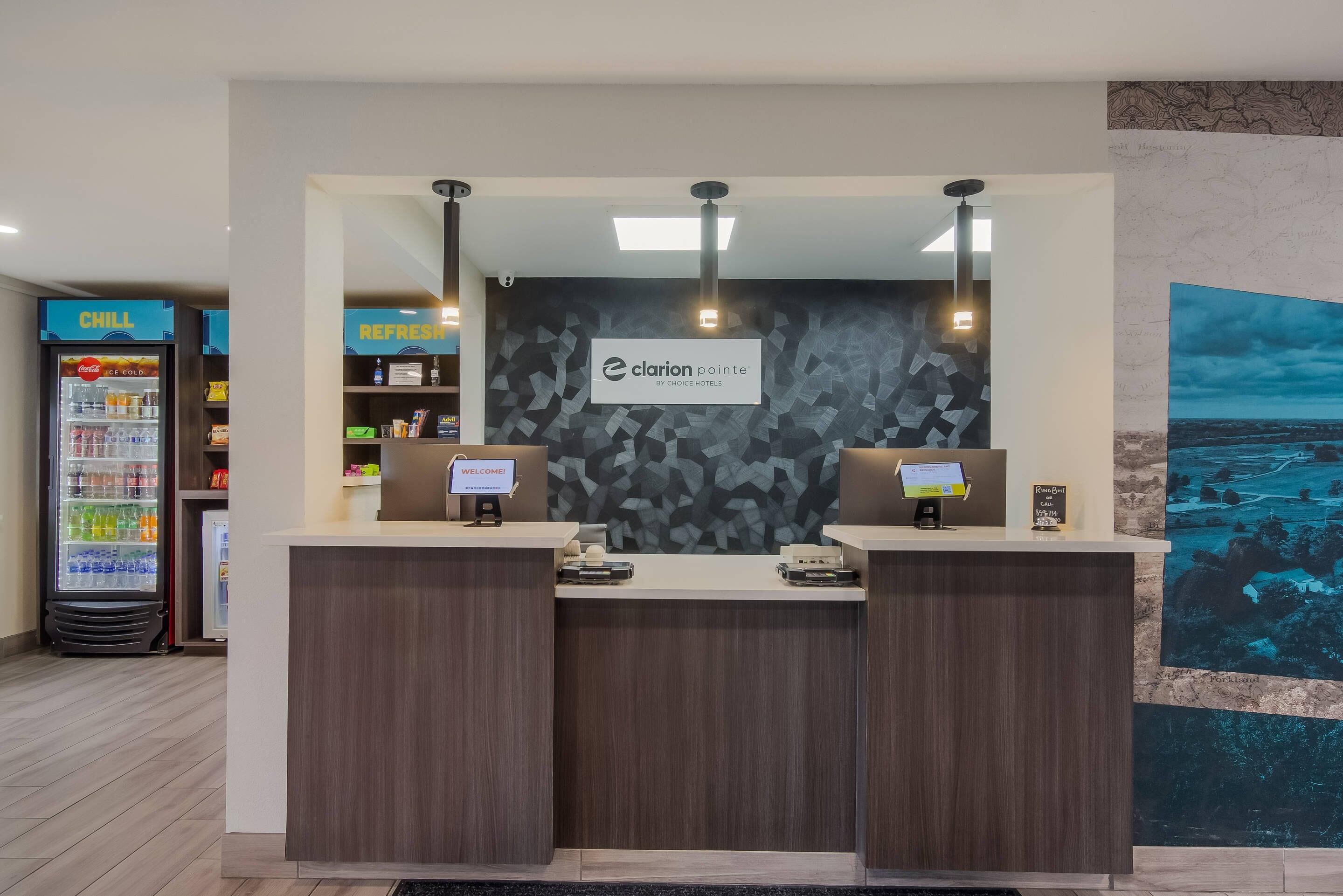 A reception desk with a 'Clarion Pointe by Choice Hotels' sign, a 'Welcome' sign, and a 'Rain Room' sign.