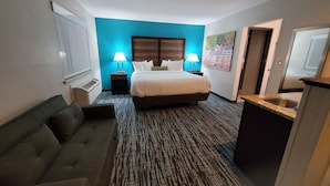 Une chambre d’hôtel avec un grand lit, deux lampes de chevet, un canapé, un petit bureau avec un lavabo et un tableau au mur.