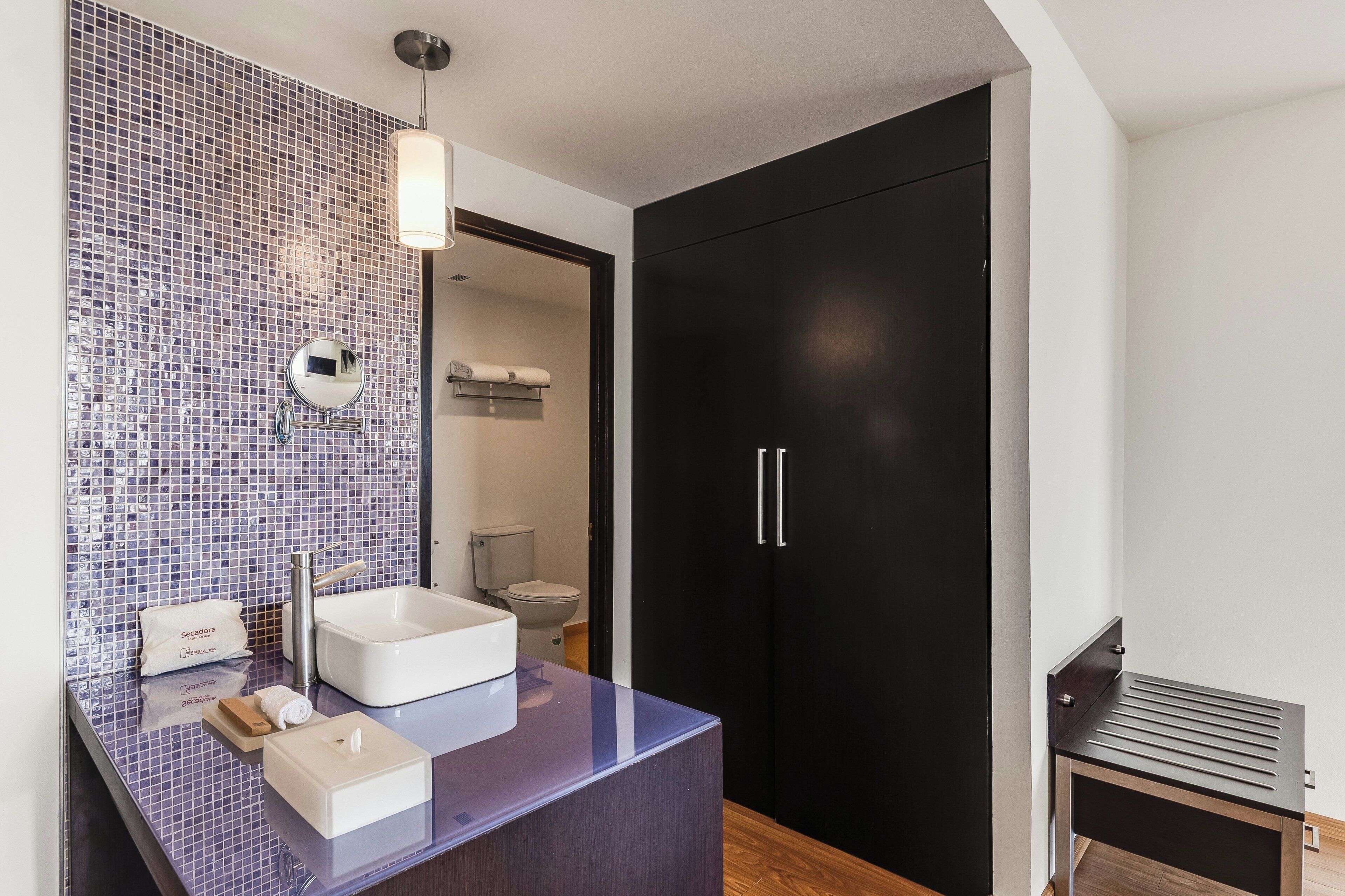 A modern bathroom with a mosaic tile backsplash, a white sink, a mirror, and a black wardrobe.
