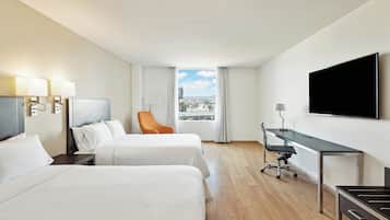 Habitación de hotel con dos camas, un escritorio, un televisor y vista a la ciudad.