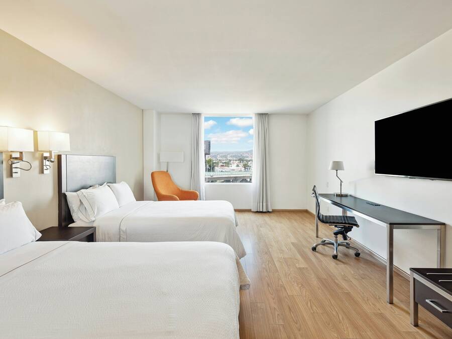 Habitación de hotel con dos camas, un escritorio, un televisor y vista a la ciudad.