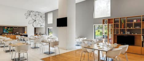 Un comedor amplio con sillas y mesas modernas, un televisor de pantalla plana en la pared y una estantería con diversos objetos.