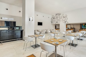 Uma sala de jantar moderna com cadeiras e mesas brancas, e uma parede decorativa central com padrão floral.