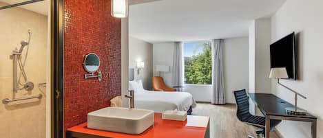 A hotel room with a bathroom, a bed, a desk, and a TV.