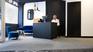 Una zona de recepción moderna con un escritorio negro, una silla azul y una alfombra estampada.