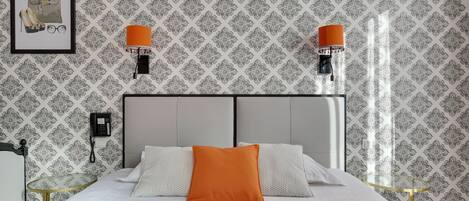 A neatly arranged hotel room with a bed, two bedside lamps, a framed picture, a telephone, and a small table.