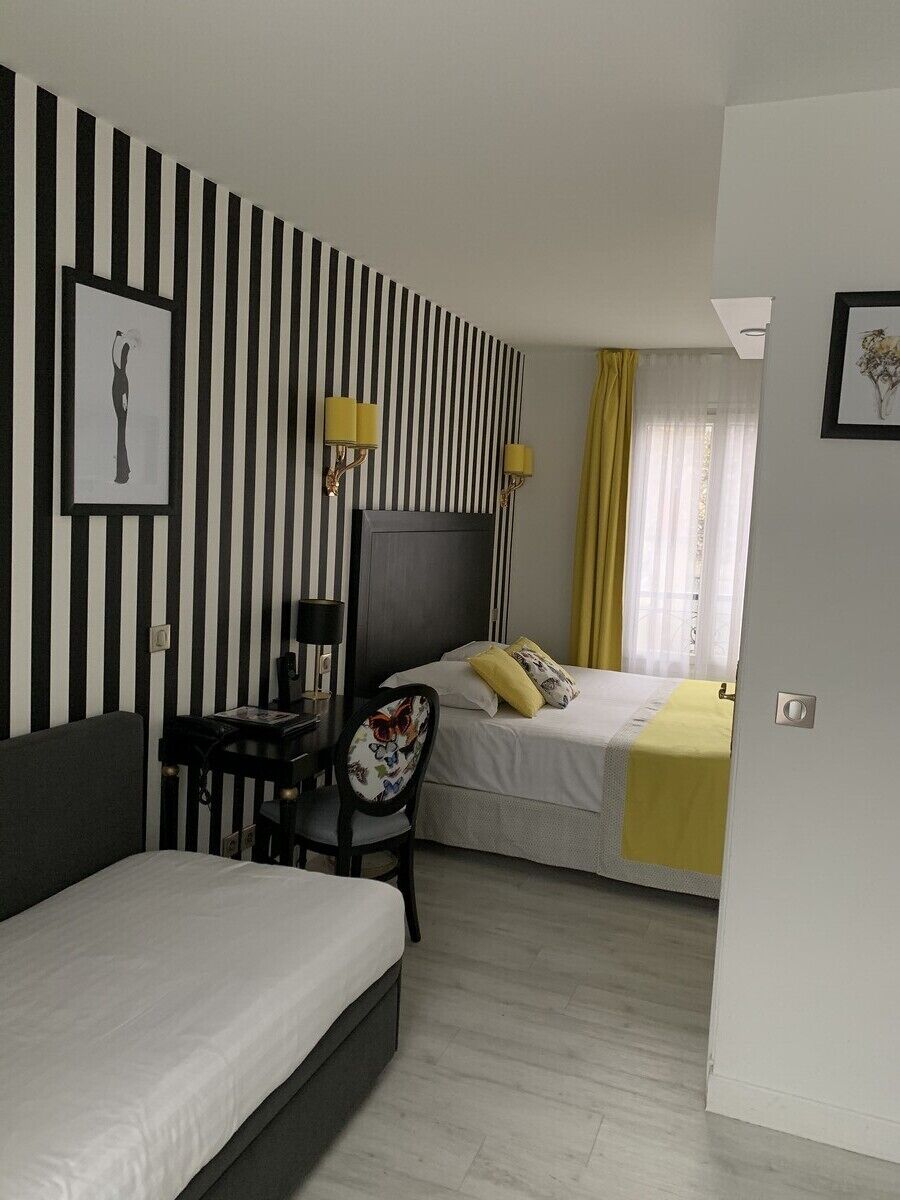 A hotel room with a striped wall, a bed, a desk with a chair, and a window with curtains.