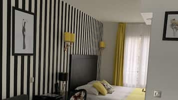 A hotel room with a striped wall, a bed, a desk with a chair, and a window with curtains.