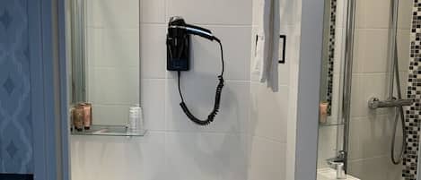 Un baño con inodoro, lavamanos y ducha. Hay un perchero con toallas, un secador de pelo y un dispensador de papel higiénico.