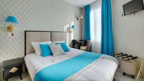 A hotel room with a neatly made bed, a small desk, a chair, and a TV mounted on the wall. - Hotel Riviera Elysées (Paris)